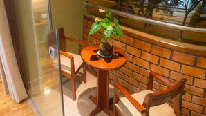 Un pequeño balcón con una mesa redonda de madera, dos sillas y una planta en maceta.