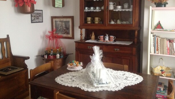 A dining area with a wooden table, chairs, a lace tablecloth, a cabinet with glass doors, and various decorative items. - B&B Relax (Miane)