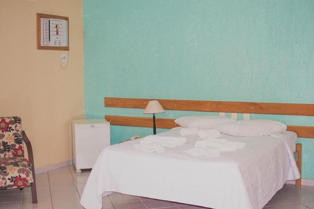 A bedroom with a bed, a nightstand, a chair, and a wall-mounted thermometer.