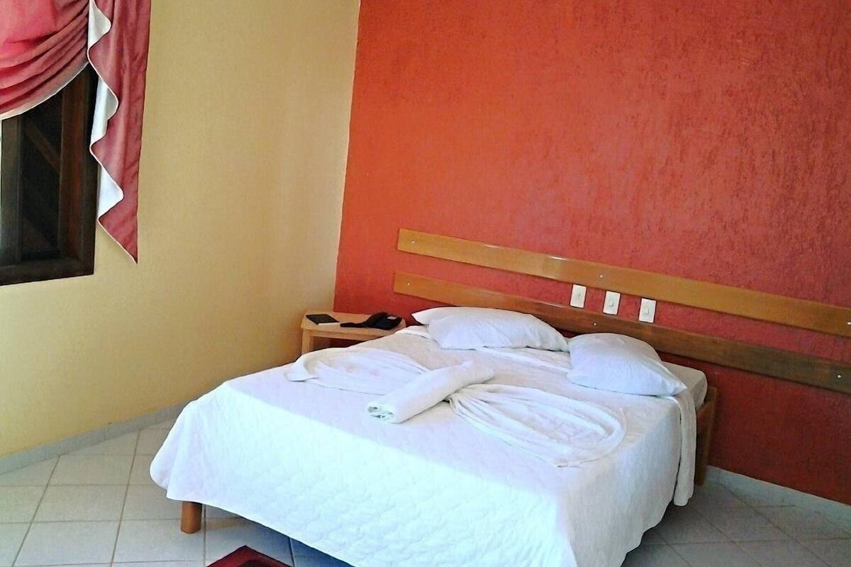 A hotel room with a bed, a nightstand, and a red rug.