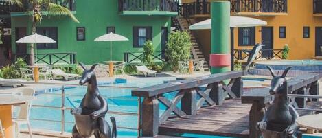 A pool area with a dolphin statue, lounge chairs, and a wooden deck.