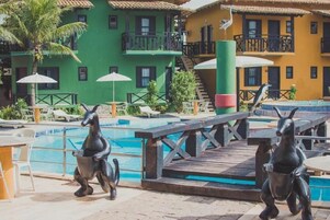 Área de piscina com estátua de golfinho, espreguiçadeiras e deck de madeira.