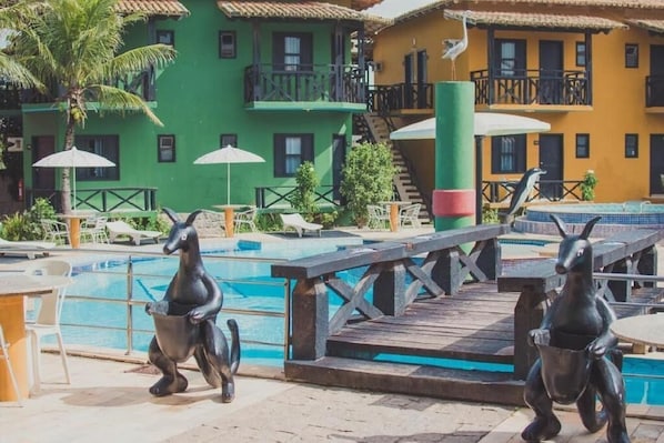 Un área de piscina con una estatua de delfín, sillas de descanso y una terraza de madera.