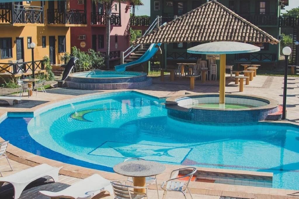 A swimming pool with a slide, lounge chairs, and a covered seating area.