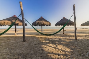 Una playa con sombrillas de paja y una hamaca.