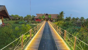 A wooden bridge leading to a building with a thatched roof, surrounded by lush greenery. - Carnaubinha Praia Resort (Luis Correia)