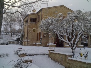 A stone building with a sloped roof and multiple windows, surrounded by snow-covered trees and ground. - Bed & Breakfast La Casa Delle Rondini (Staffolo)