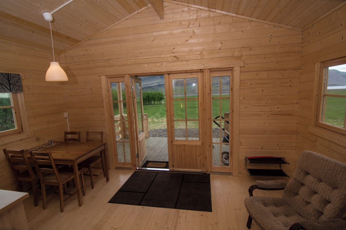 En stuga byggd av trä med ett matområde, en soffa och utsikt över naturen.