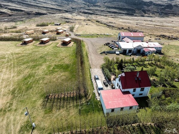Vue aérienne d’une propriété rurale comprenant plusieurs bâtiments, dont une maison principale avec un toit rouge, une grange et plusieurs petites constructions. On aperçoit un vignoble au premier plan et un chemin de terre reliant les différents bâtiments.