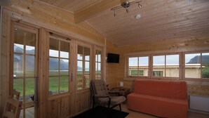 A wooden cabin with large glass doors, a sofa, a chair, and a small table. - Bragdavellir Cottages (Djupivogur)