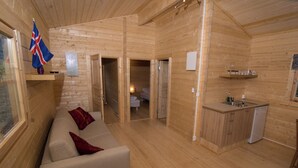 A wooden cabin interior with a sofa, a small kitchen area, and a bathroom visible through an open door. - Bragdavellir Cottages (Djupivogur)