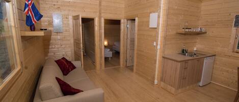 A wooden cabin interior with a sofa, a small kitchen area, and a bathroom visible through an open door.