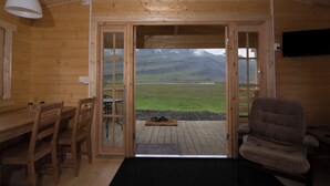 A wooden interior with a dining table and chairs, a sofa, and a television on the wall. - Bragdavellir Cottages (Djupivogur)