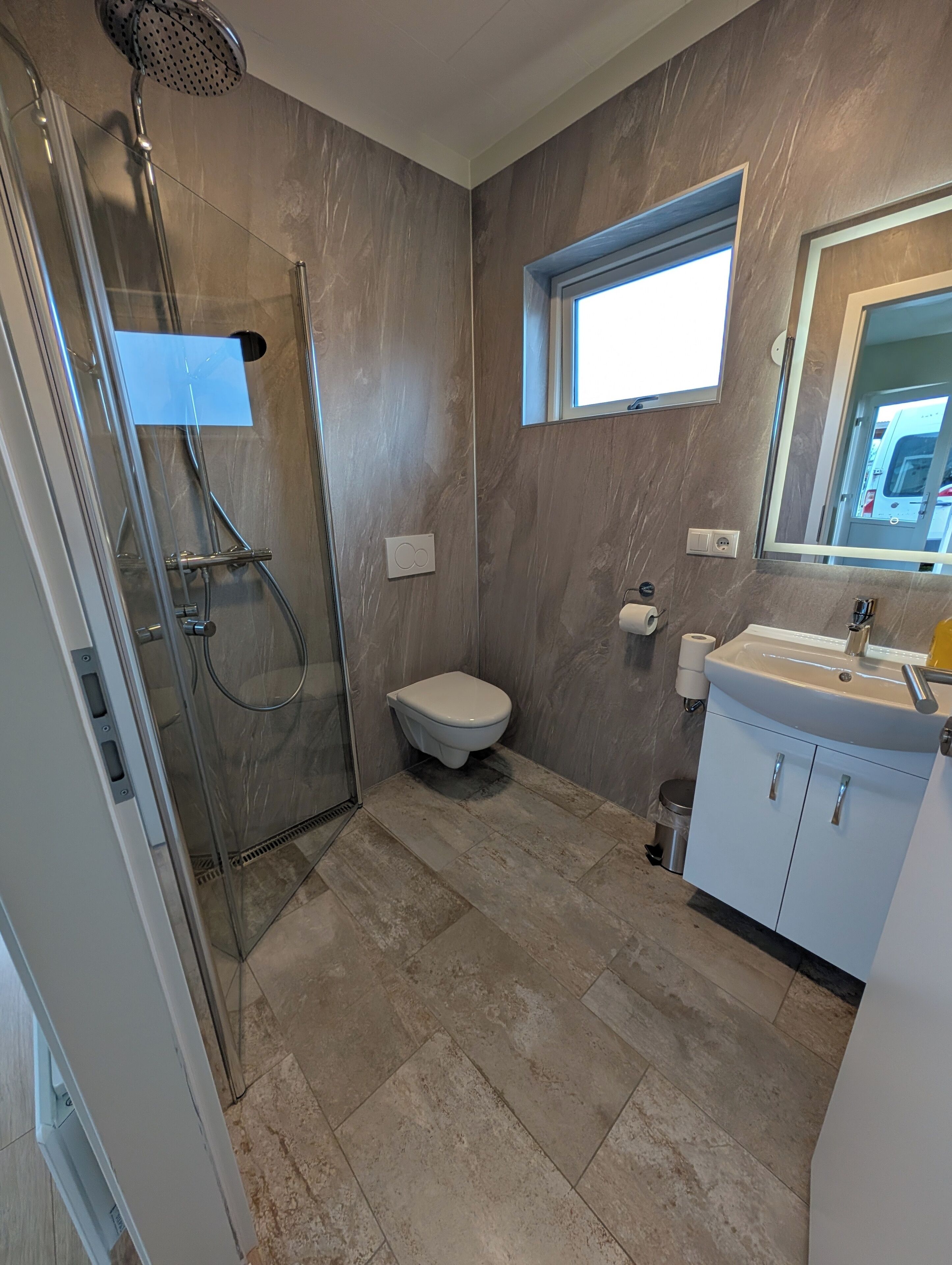 A modern bathroom with a glass-enclosed shower, a toilet, and a sink with a mirror above it.