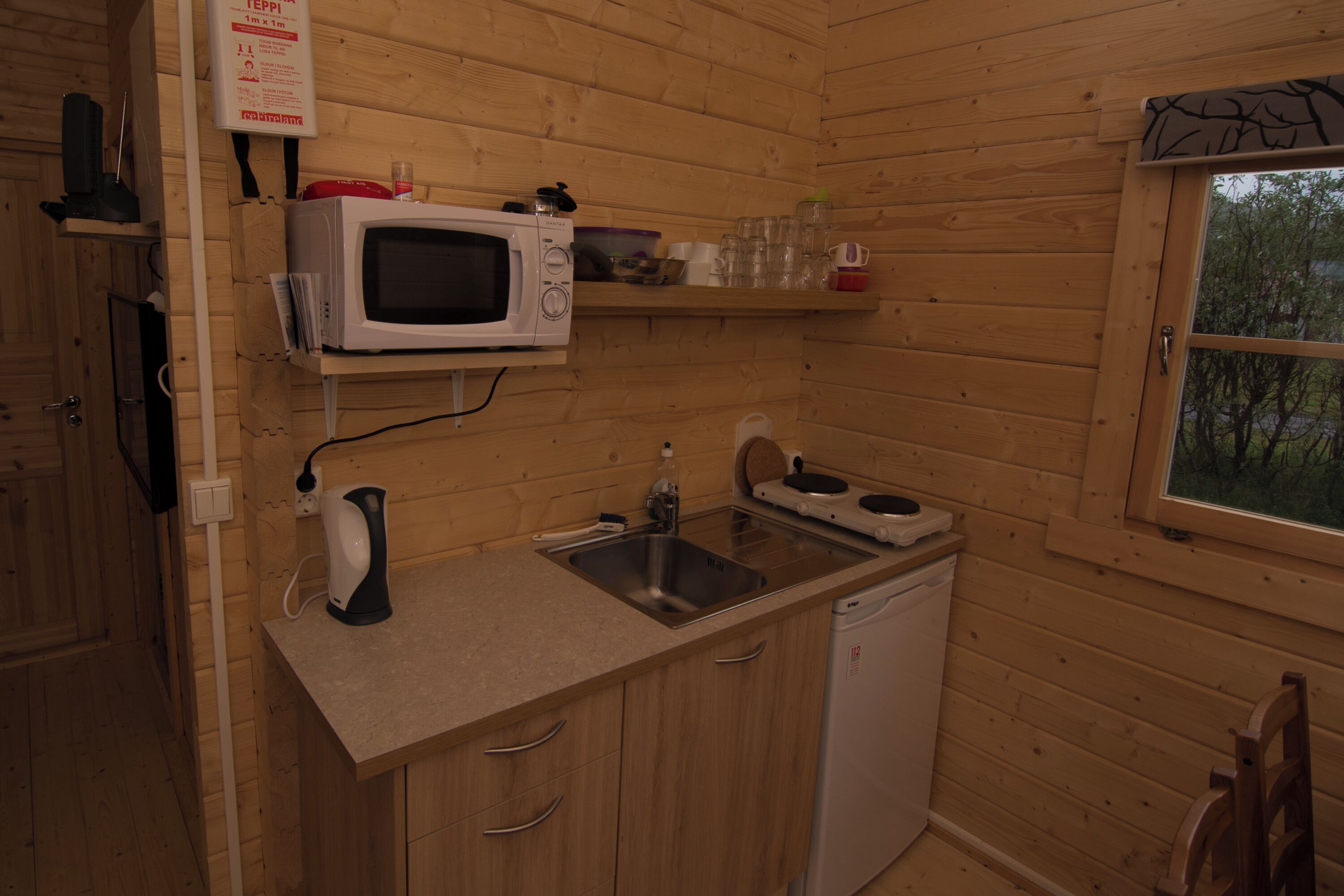 A compact kitchen with wooden walls, a microwave, a sink, and a dishwasher.
