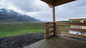 A wooden structure with a view of a grassy field and mountains in the background. - Bragdavellir Cottages (Djupivogur)