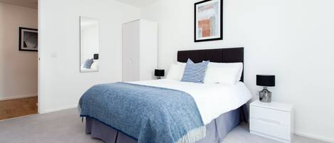 A modern bedroom with a bed, bedside tables, a wardrobe, and a framed picture on the wall.