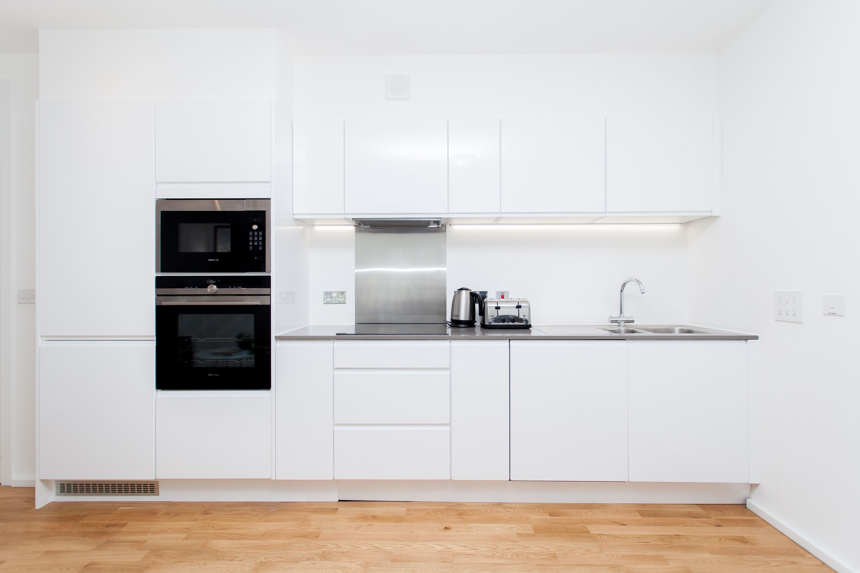 A modern kitchen with white cabinetry, a double oven, a coffee maker, and a stainless steel sink.