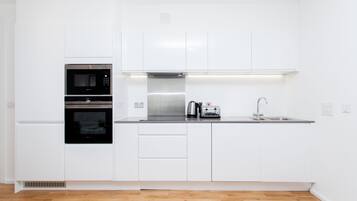 A modern kitchen with white cabinetry, a double oven, a coffee maker, and a stainless steel sink.