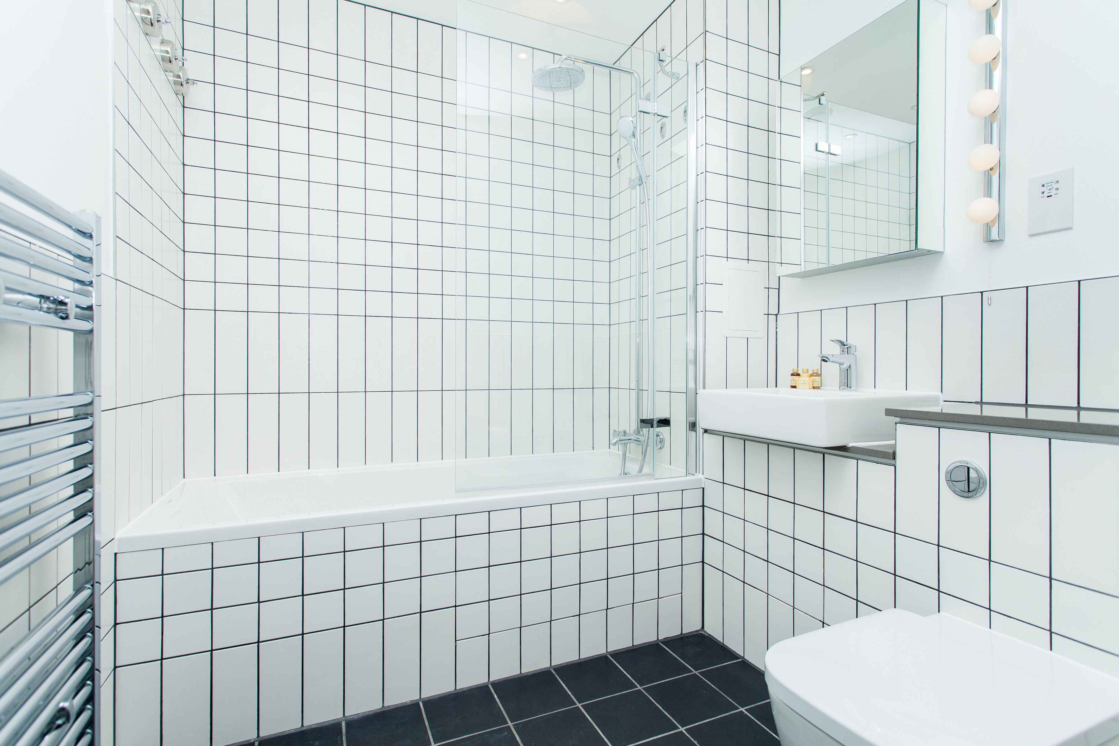 A modern bathroom with white tiles, a bathtub, a toilet, and a shower.