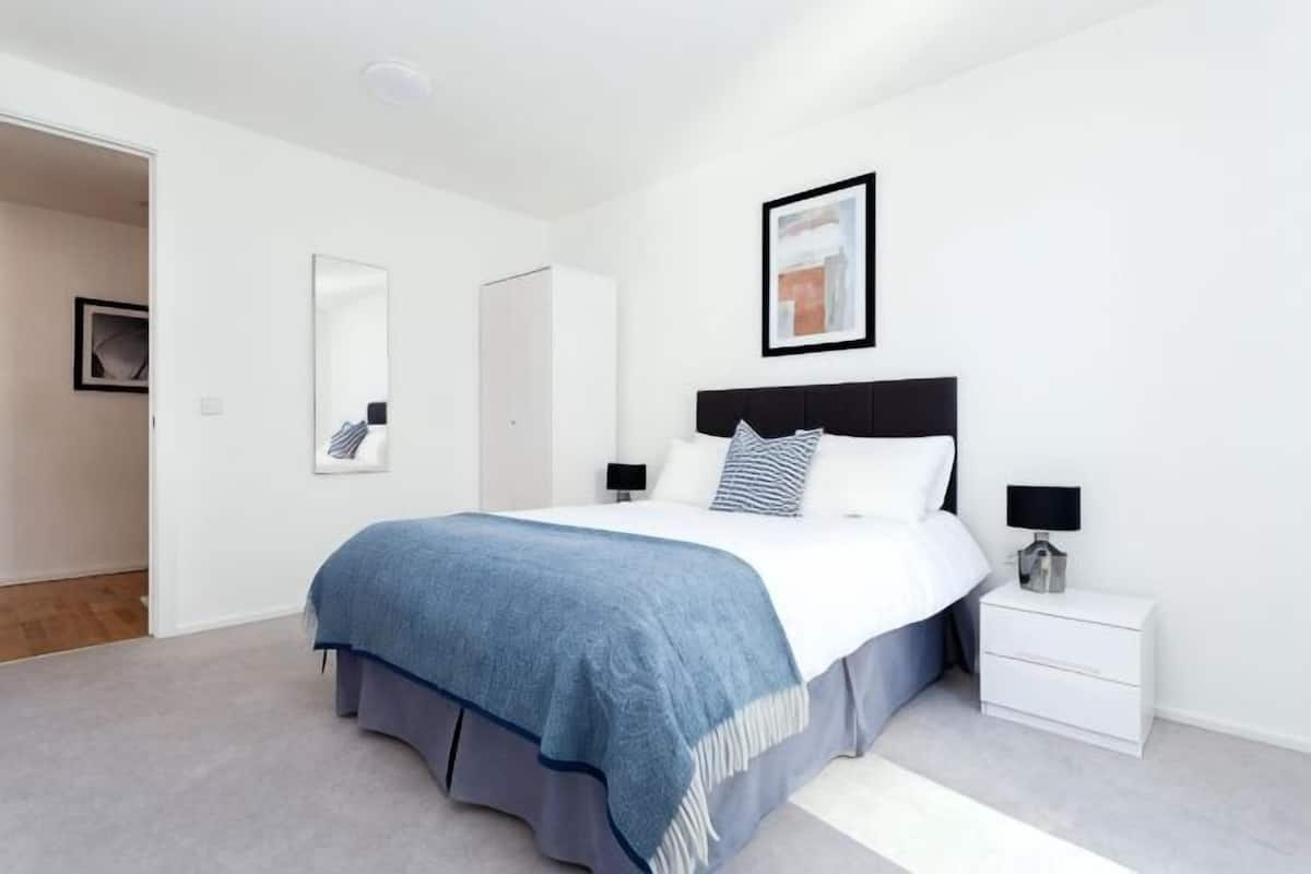 Une chambre à coucher avec un lit, des tables de chevet, une commode, un miroir et un tableau encadré accroché au mur.