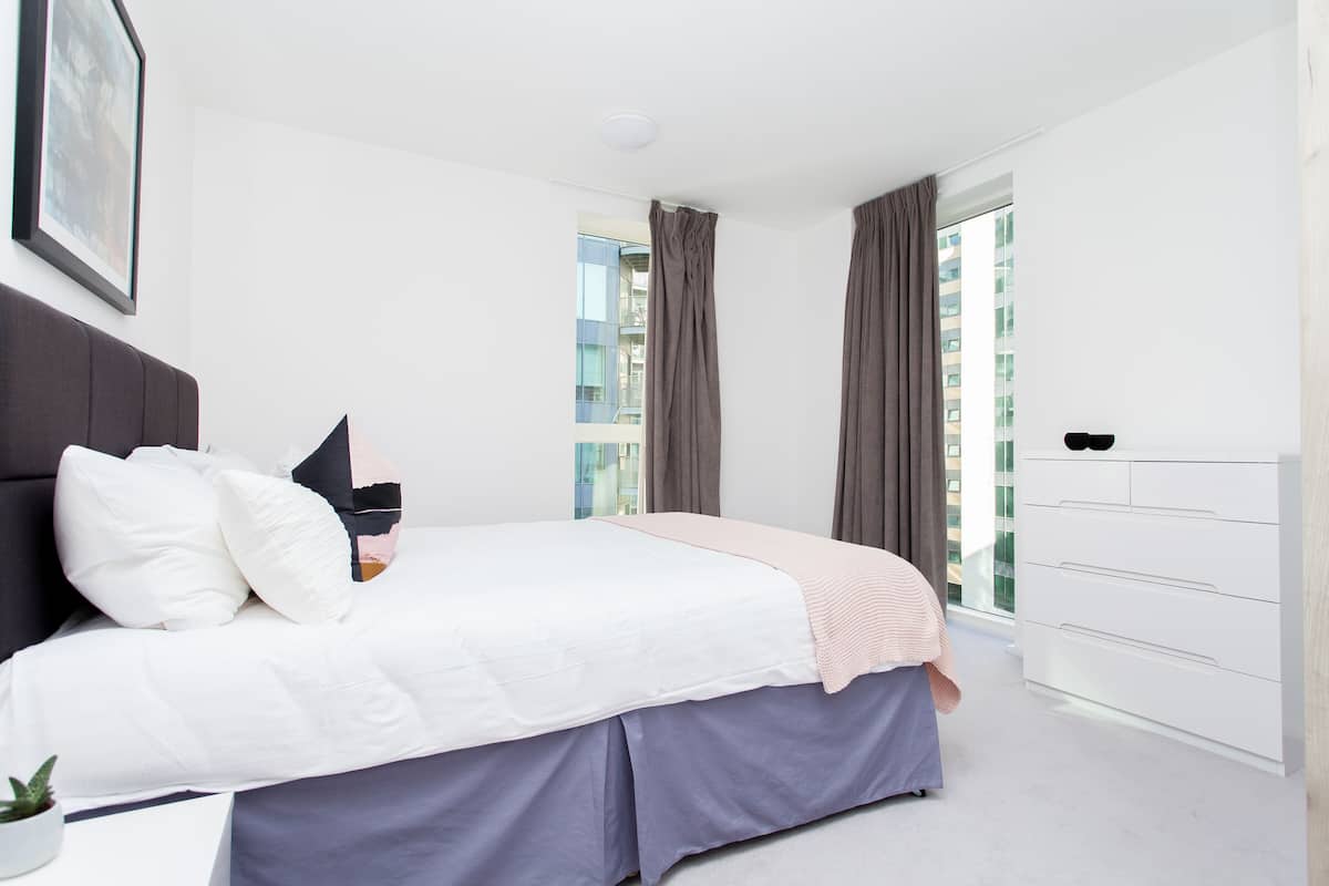 Une chambre à coucher avec un lit, une commode, une fenêtre avec des rideaux et une plante.