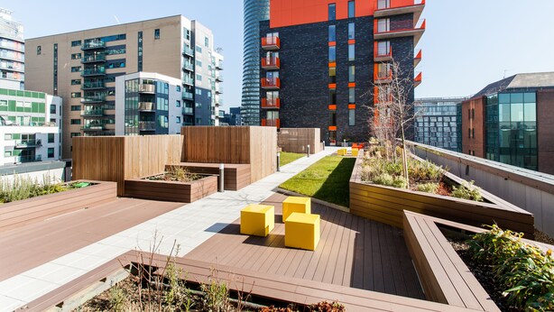 A rooftop terrace with wooden planters, yellow seating, and a view of surrounding buildings. - Clover Court by Aeria Apartments (London)