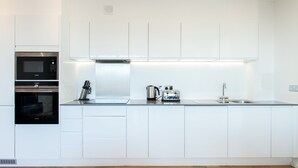 A modern kitchen with white cabinetry, a built-in microwave, oven, and a stainless steel sink. - Clover Court by Aeria Apartments (London)