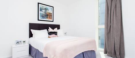 A bedroom with a bed, a nightstand, a framed picture, and a window with curtains.