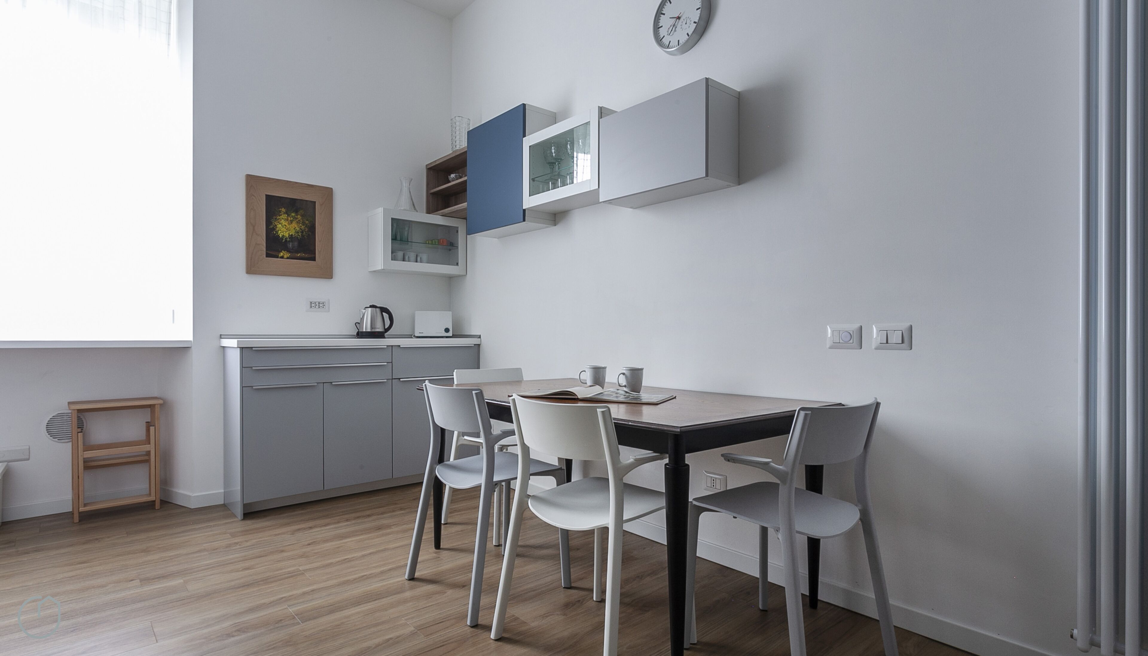 Une cuisine moderne avec des meubles blancs, une table à manger en bois et quatre chaises blanches.