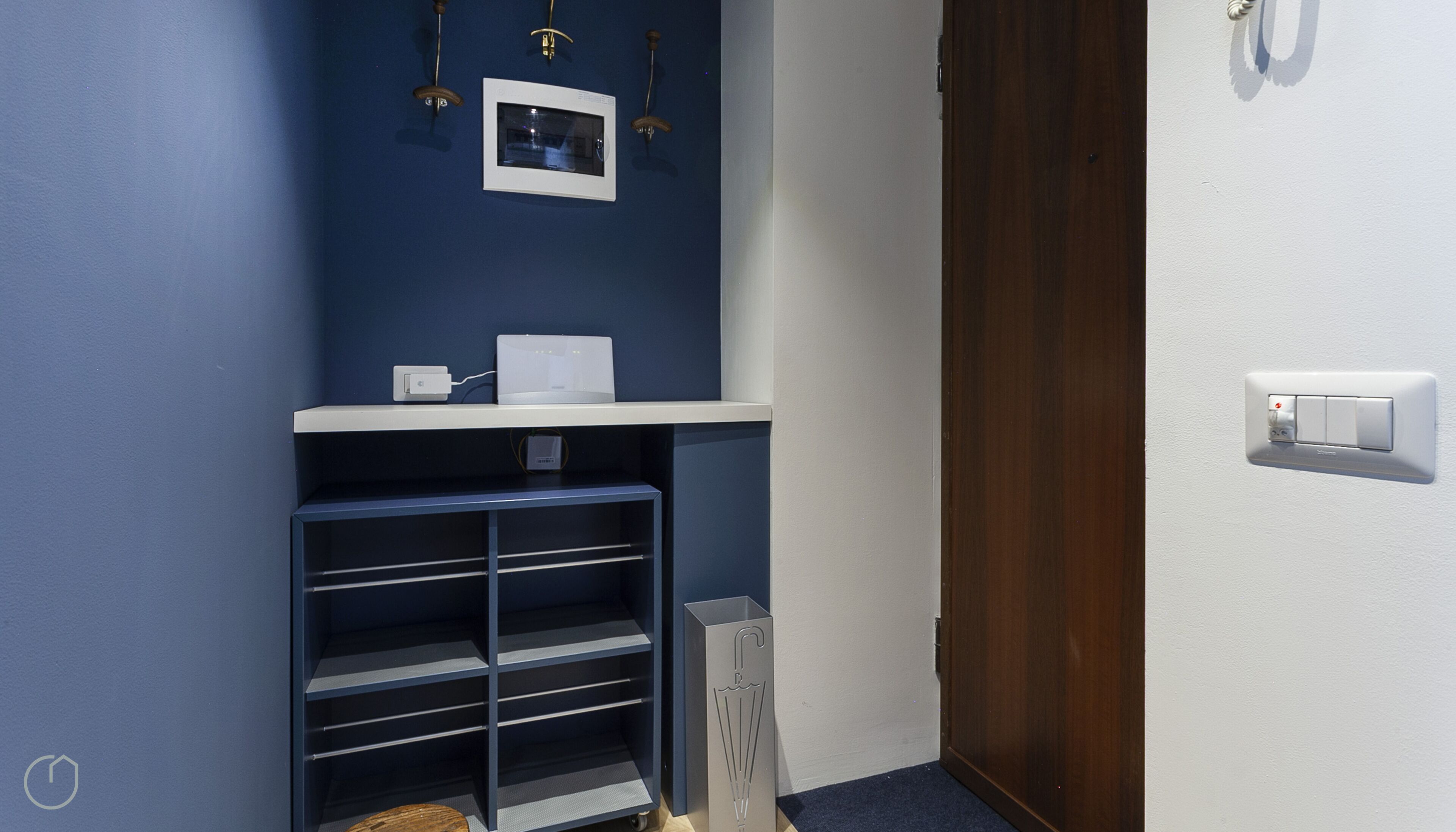 A bathroom with a blue wall, a white shelf, a towel rack, a shower, and a door.