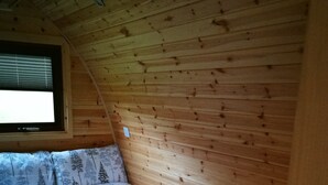 A bedroom with a wooden sloped ceiling, a bed with a floral-patterned bedspread, and a window with blinds. - Cosy Camping Suffolk (Ipswich)