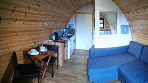 A cozy cabin interior with a dining area, a sofa, and a kitchen. - Cosy Camping Suffolk (Ipswich)