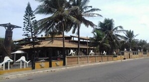 A building with a thatched roof, palm trees, and a fence with decorative elements.