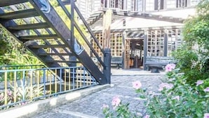 A cobblestone courtyard with a wooden staircase, a bench, and a building with large windows.