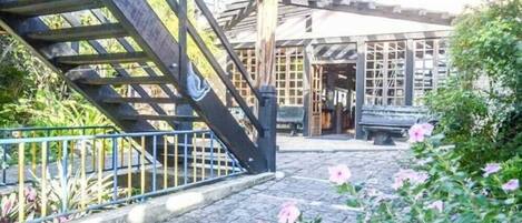 A cobblestone courtyard with a wooden staircase, a bench, and a building with large windows.