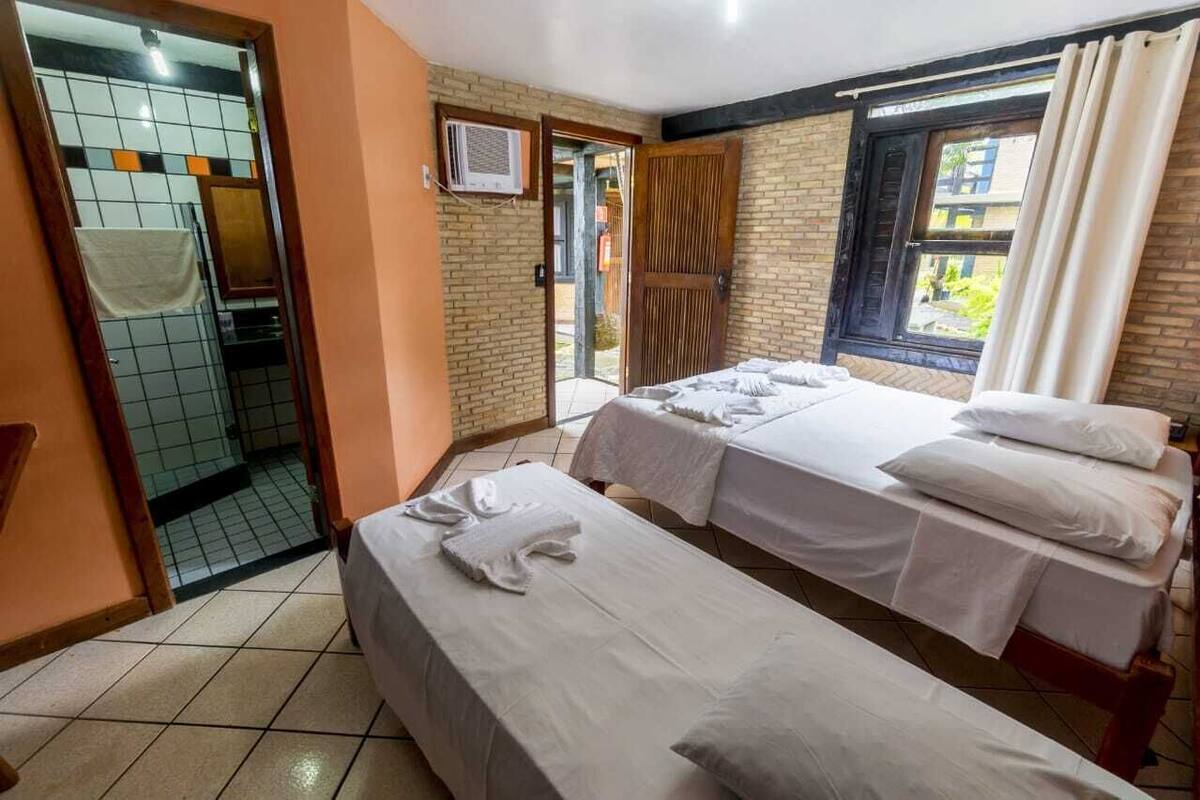 Une chambre d’hôtel avec deux lits, une salle de bain avec douche et une fenêtre avec des rideaux.