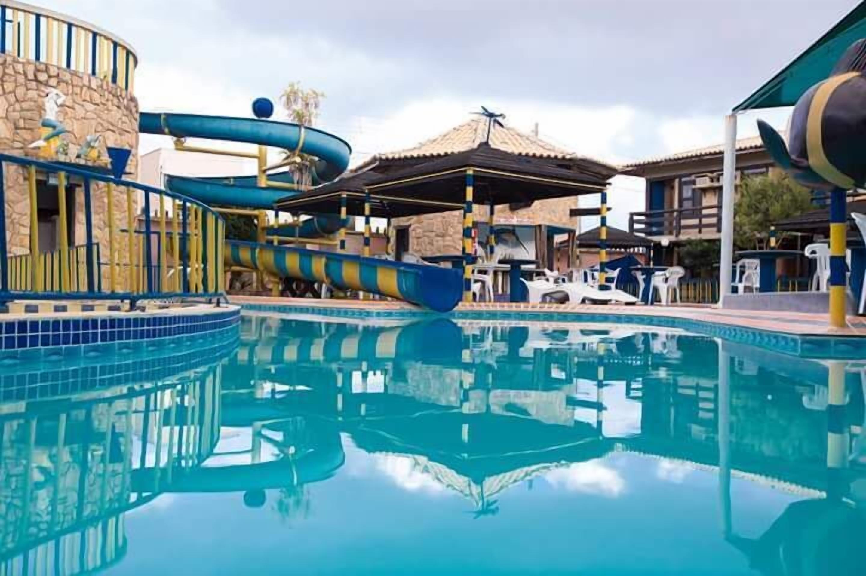 A swimming pool with a water slide, lounge chairs, and a covered area.