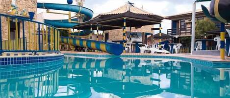 A swimming pool with a water slide, lounge chairs, and a covered area.