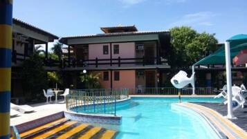 A swimming pool with a blue water feature, a multi-story building with balconies, and outdoor seating areas.