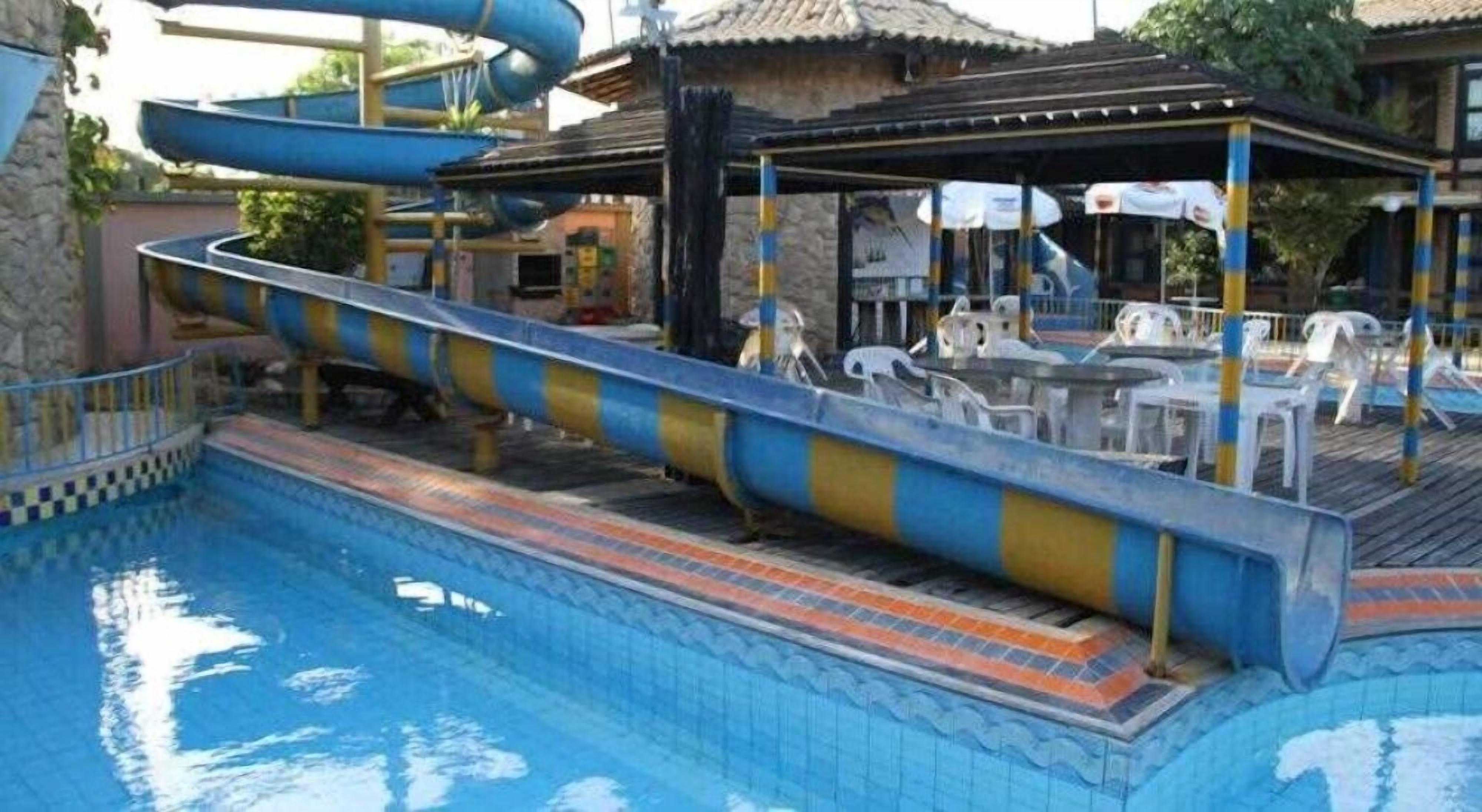 Un área de piscina con tobogán de agua, sillones de descanso y una zona de estar cubierta.