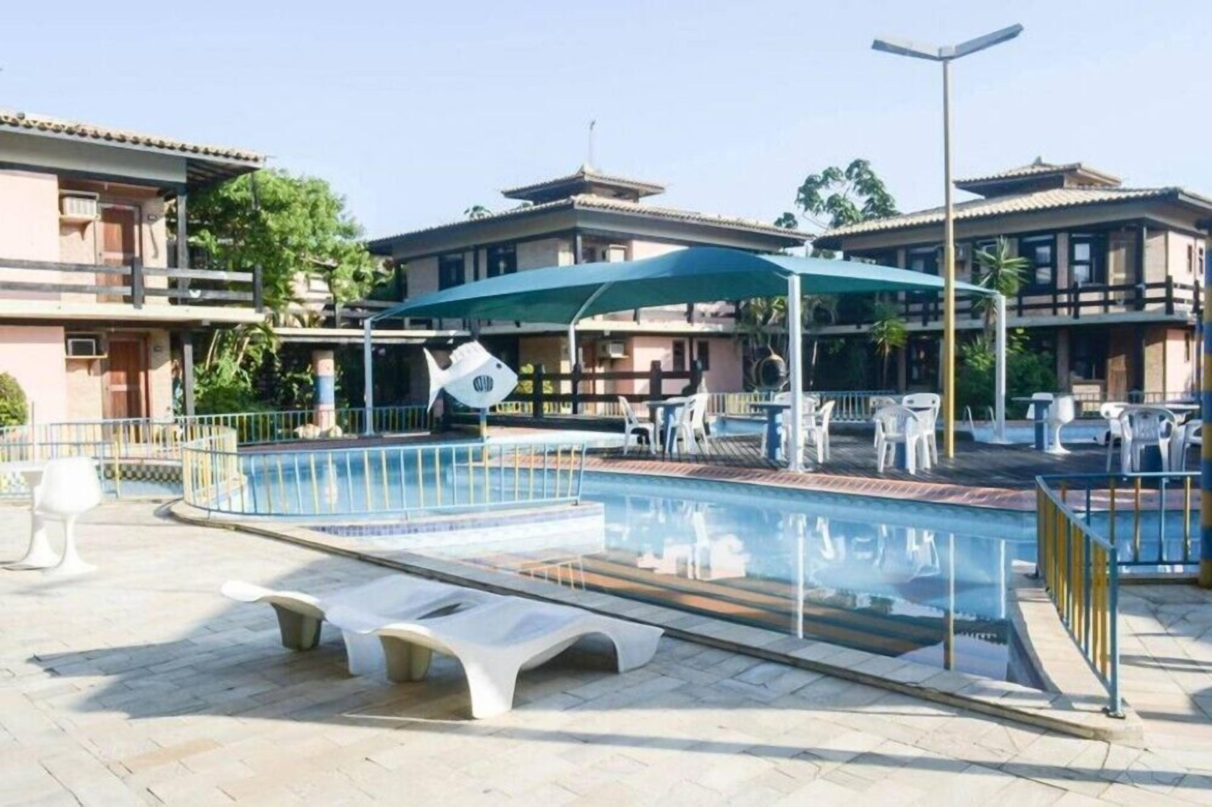A swimming pool with lounge chairs and umbrellas, surrounded by buildings with balconies.