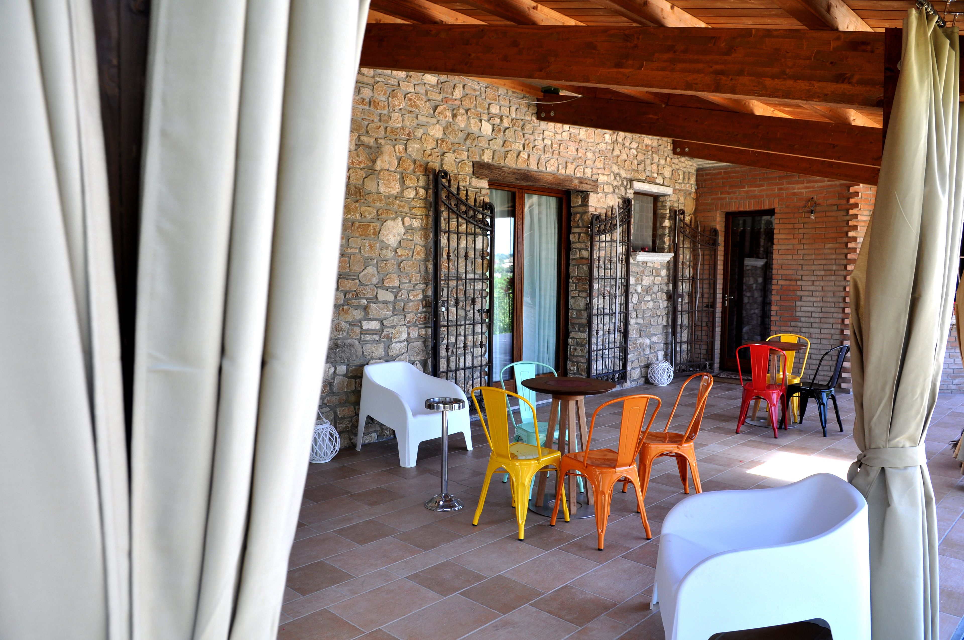 Une terrasse extérieure avec des murs en pierre, un plafond en bois, ainsi que des chaises et des tables en plastique de couleurs vives.
