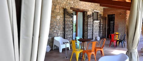 Une terrasse extérieure avec des murs en pierre, un plafond en bois, ainsi que des chaises et des tables en plastique de couleurs vives.