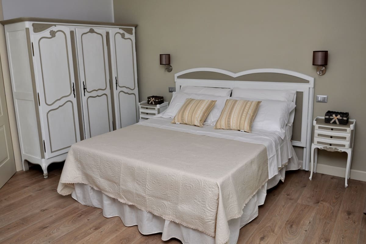 Une chambre à coucher avec un grand lit, une armoire blanche, des tables de chevet et des lampes fixées au mur.