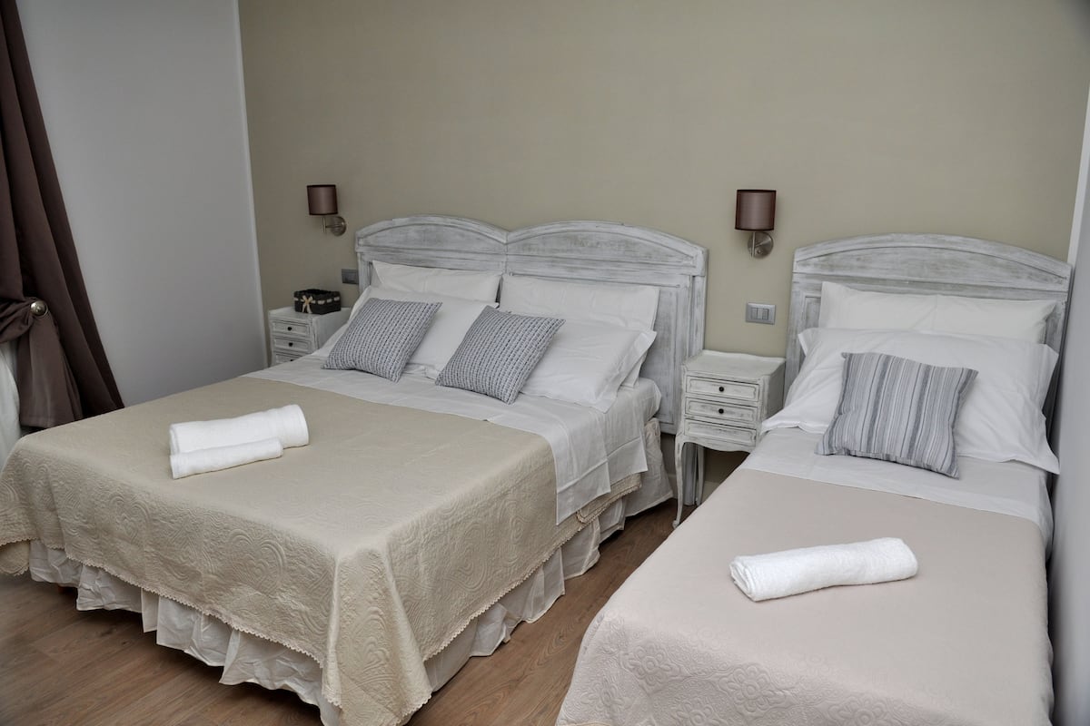 Une chambre d’hôtel avec deux lits, chacun recouvert d’une courtepointe blanche et doté d’oreillers, une table de chevet avec une lampe et un plancher en bois.
