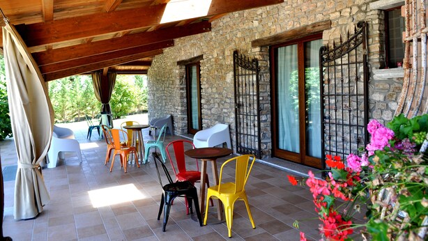 Un patio cubierto con paredes de piedra, vigas de madera y una variedad de sillas y mesas.
