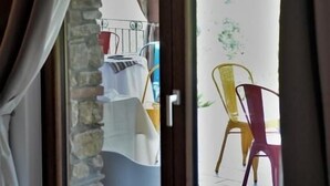 Vista a través de una puerta de cristal que muestra un cuarto con pared de piedra, una cama con cubrecama blanco y una mesa con sillas.