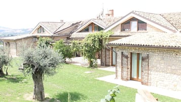 A row of stone buildings with sloped roofs, a grassy courtyard, and a tree.