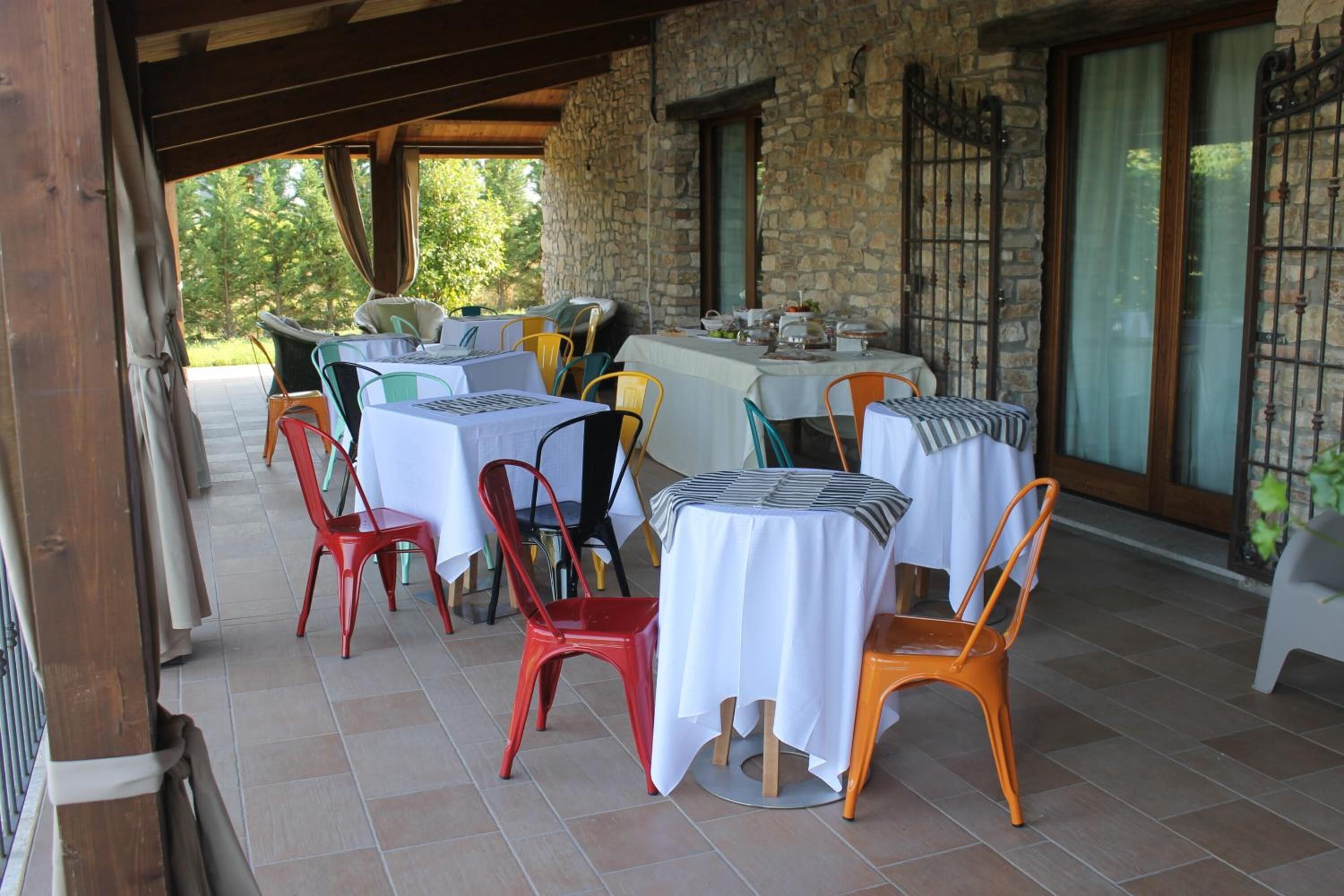 An outdoor dining area with multiple tables and chairs, stone walls, and large windows.